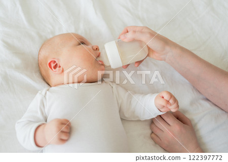 Happy family at home. Mother hand nursing feeding little baby toddler child milk from bottle. Newborn Infant baby girl sucking eating drinking milk. Mom of breast feeding baby. Motherhood happy child Happy family at home. Mother hand nursing feeding little baby toddler child milk from bottle. Newborn Infant baby girl sucking eating drinking milk. Mom of breast feeding baby. Motherhood happy child 122397772