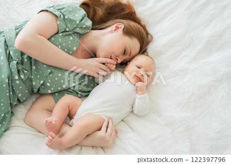 Happy family at home. Mother playing with little toddler child on bed. Mom baby relax playing having fun together. Mother hugs baby with love care. Mom of breast feeding baby rest in living room Happy family at home. Mother playing with little toddler child on bed. Mom baby relax playing having fun together. Mother hugs baby with love care. Mom of breast feeding baby rest in living room 122397796