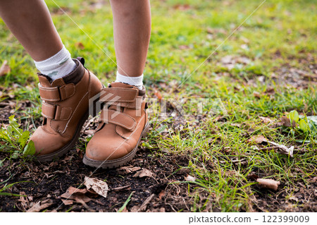 Childs feet in brown boots on grass with autumn leaves 122399009