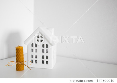 Minimalist decor with ceramic house and rolled beeswax candle on white surface 122399010