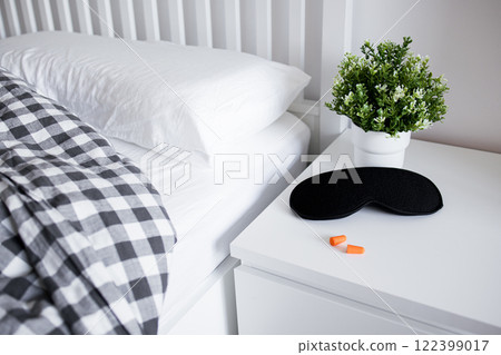 Cozy bedroom setup with sleep mask, earplugs, and plant on white nightstand Cozy bedroom setup with sleep mask, earplugs, and plant on white nightstand 122399017