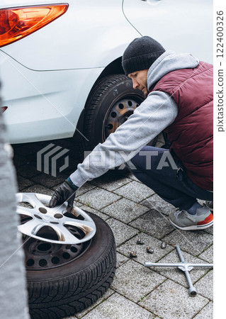 Man replacing his car tire with winter tires using a wrench, preparing for the cold weather Man replacing his car tire with winter tires using a wrench, preparing for the cold weather 122400326
