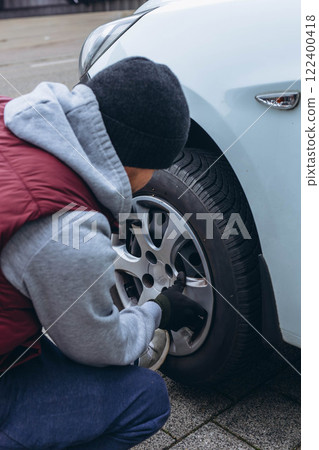 Man changing his car's tire with a wrench, replacing it with winter tires for the season 122400418