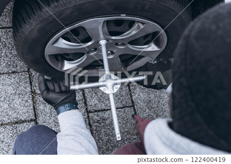 Man changing his car's tire with a wrench, replacing it with winter tires for the season 122400419