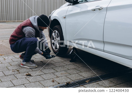 Young man changing a car tire on the road, using a wrench to unscrew the lug nuts 122400430