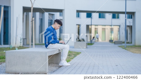 Focused student working on laptop outside university building Focused student working on laptop outside university building 122400466