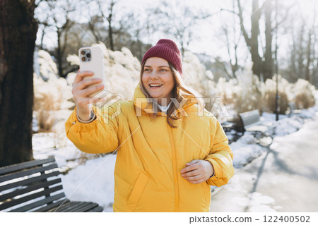 Smiling woman in winter clothing taking photo on park background. Selfie time. Holidays, rest, blogging banner. Charming female wearing stylish outfit have fine Smiling woman in winter clothing taking photo on park background. Selfie time. Holidays, rest, blogging banner. Charming female wearing stylish outfit have fine 122400502