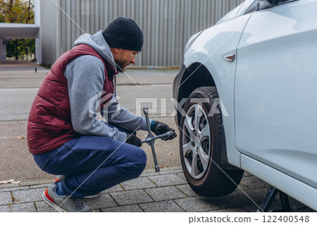 Man changing his car's tire with a wrench, replacing it with winter tires for the season Man changing his car's tire with a wrench, replacing it with winter tires for the season 122400548