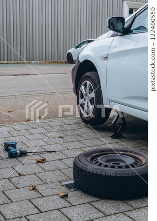 Man changing his car's tire with a wrench, replacing it with winter tires for the season Man changing his car's tire with a wrench, replacing it with winter tires for the season 122400550