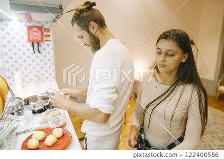 A couple happily cooking together in a beautifully modern kitchen with natural sunlight A couple happily cooking together in a beautifully modern kitchen with natural sunlight 122400586