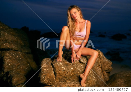 Woman in bikini on night beach. Model poses on rocks by ocean in moonlight. Perfect for dating app mockups, fashion ads, editorial beauty. Stunning beach scene for lifestyle, travel, summer. Woman in bikini on night beach. Model poses on rocks by ocean in moonlight. Perfect for dating app mockups, fashion ads, editorial beauty. Stunning beach scene for lifestyle, travel, summer. 122400727