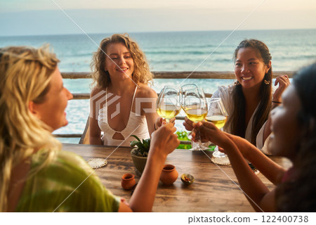 Group of diverse women cheers wine glasses at seaside restaurant. Happy friends toast at sunset dining. Relaxation and joy on vacation by ocean. Wine party celebrates togetherness. Group of diverse women cheers wine glasses at seaside restaurant. Happy friends toast at sunset dining. Relaxation and joy on vacation by ocean. Wine party celebrates togetherness. 122400738