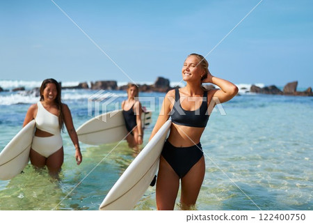 Three women in swimwear carry surfboards through clear ocean water on sunny beach. Smiling, they enjoy active lifestyle. Summer surf adventure promotes wellbeing, fitness, bonding, nature. Three women in swimwear carry surfboards through clear ocean water on sunny beach. Smiling, they enjoy active lifestyle. Summer surf adventure promotes wellbeing, fitness, bonding, nature. 122400750
