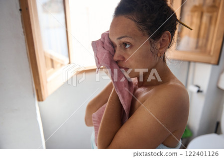 Woman drying her face with a towel in a bright bathroom scene 122401126