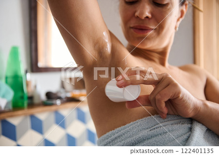 Woman applying deodorant in a bathroom after showering Woman applying deodorant in a bathroom after showering 122401135
