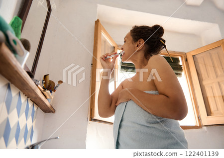 Woman brushing teeth in natural light in her cozy home 122401139