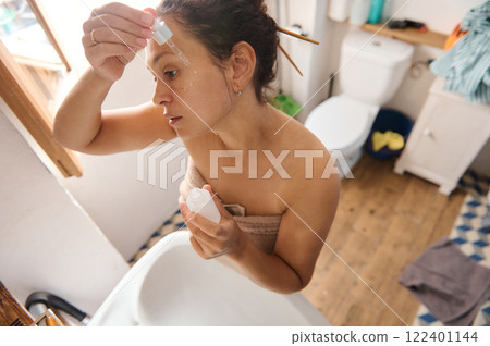 Woman applying skincare serum in a cozy bathroom setting 122401144