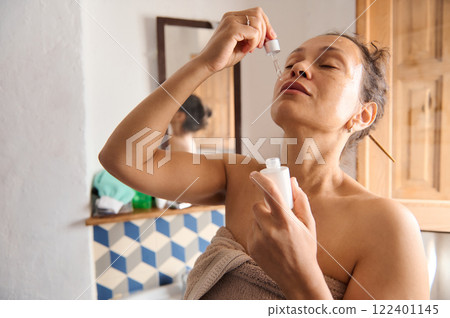 Woman applying skincare serum to her face in a natural light bathroom Woman applying skincare serum to her face in a natural light bathroom 122401145