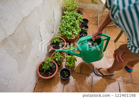 Person watering potted plants on a balcony with a green watering can Person watering potted plants on a balcony with a green watering can 122401198