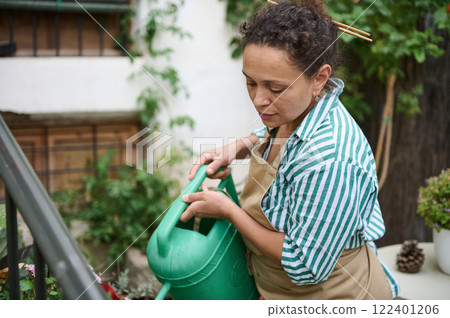 Woman watering plants in an outdoor garden with a green watering can 122401206