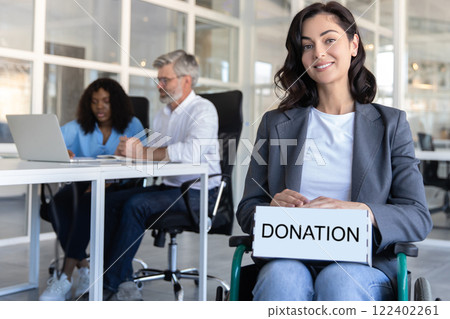 Disabled female worker doing her job in office environment holding box with donation inscription 122402261