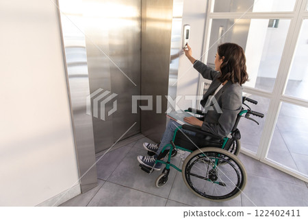 Businesswoman in wheelchair in corporate office using touch panel to operate the lift 122402411