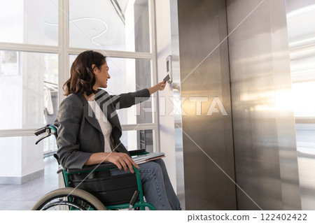 Businesswoman in wheelchair in corporate office using touch panel to operate the lift 122402422