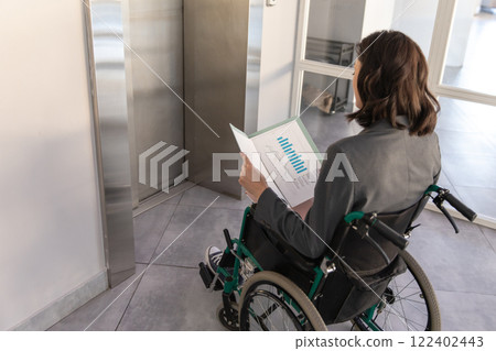 Businesswoman in wheelchair studies documents while waiting the elevator in the company Businesswoman in wheelchair studies documents while waiting the elevator in the company 122402443