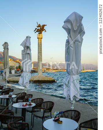 Adriatic Riviera, Kastel Stari waterfront promenade with cafe tables, monument with a horseman 122402672