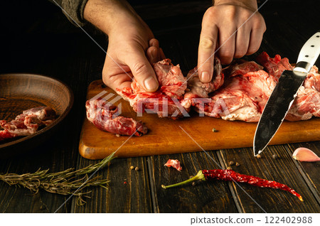 Hands skillfully prepare fresh cuts of meat on a wooden board, surrounded by aromatic herbs and spices. The warm hues of the kitchen create an inviting atmosphere for culinary creativity Hands skillfully prepare fresh cuts of meat on a wooden board, surrounded by aromatic herbs and spices. The warm hues of the kitchen create an inviting atmosphere for culinary creativity 122402988