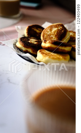 A woman forks fluffy golden pancakes with crispy edges while coffee is in the background out of focus breakfast concept morning meal with pancakes coffee and fork casual dining brunch at home 122403499