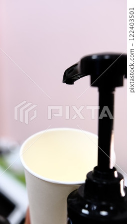 Barista adds red cherry syrup to a white paper coffee cup using a dispenser at coffee shop creating delicious flavored drink with vibrant color perfect for coffee lovers seeking refreshing beverages 122403501