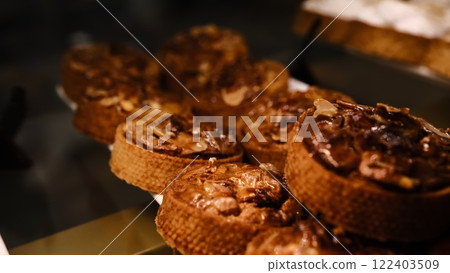 Beautiful nut tart covered glaze in shortcrust pastry shell on white plate displayed on counter fresh delicious dessert perfect for holidays parties and celebrations indulgent sweet treat with nuts 122403509