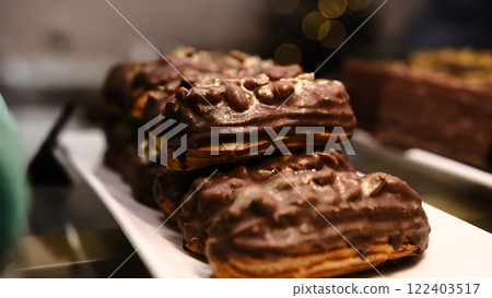 A delicious gourmet eclair filled with creamy custard, topped with crunchy peanuts, rich chocolate glaze, and a luxurious golden sprinkle, creating a visually appealing and indulgent dessert. 122403517