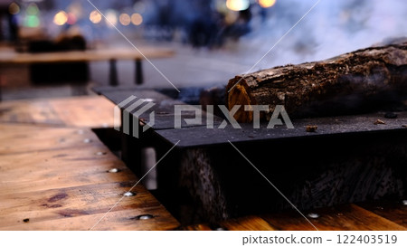 A glowing log burns gently in a stylish fire pit, creating a warm and festive atmosphere at a Christmas market while providing cozy heat for visitors on a chilly winter evening. 122403519