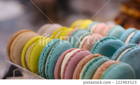 Close-up of colorful macarons with white cream filling displayed under soft lighting on a countertop with a blurred background and selective focus highlighting their delicate texture and vibrant hues 122403523