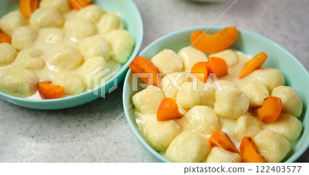 Close-up of hands decorating dumplings with sour cream and apricot on blue plate, against granite background. Ideal for food enthusiasts seeking culinary inspiration. Close-up of hands decorating dumplings with sour cream and apricot on blue plate, against granite background. Ideal for food enthusiasts seeking culinary inspiration. 122403577