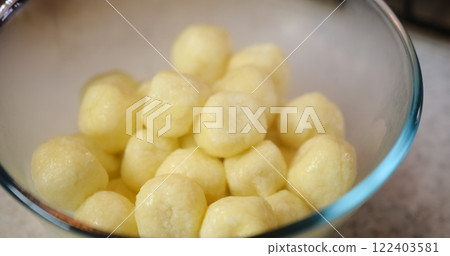 Spoon stirring hot dumplings in glass bowl with steam, set against granite background. Culinary scene captures food preparation process with vibrant colors and textures. 122403581