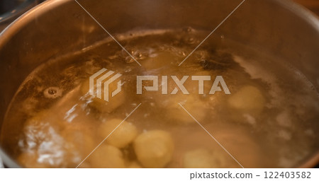 In a vibrant kitchen setting, dough balls stuffed with cheese are immersed in boiling water within a steel pan, capturing the essence of culinary artistry. This footage celebrates homemade cuisine. 122403582