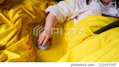 A woman's hand operates a blue wireless mouse while working in bed, illustrating the concept of remote freelance work. Freelancing from the comfort of home, using technology for remote productivity. 122403597