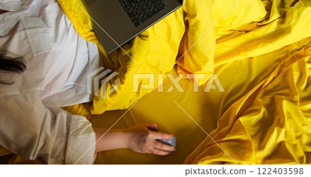 A woman's hand operates blue wireless mouse while working in bed with laptop illustrating the concept remote freelance work. Freelancing from comfort of home using technology for remote productivity. 122403598