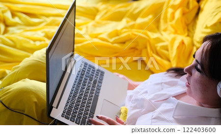 Woman in white shirt using laptop while working in cozy yellow bed at home portraying concept of freelance remote work Illustrating the modern trend flexible work environments remote productivity Woman in white shirt using laptop while working in cozy yellow bed at home portraying concept of freelance remote work Illustrating the modern trend flexible work environments remote productivity 122403600