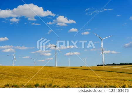 Large Modern Wind Turbines Generating Renewable Energy Against a Bright Blue Sky with Fluffy Clouds 122403673