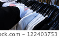 young woman browses through t-shirts on hangers in a clothing store examines each item showcasing the shopping experience variety of styles available perfect for those trendy wardrobe additions 122403753