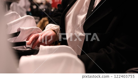 young woman browses through t-shirts on hangers in a clothing store examines each item showcasing the shopping experience variety of styles available perfect for those trendy wardrobe additions 122403755