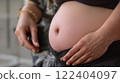 A beautiful expecting mother gently cradling her baby bump in soft, natural light 122404097