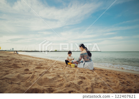 happy toddler baby girl playing sand toy with mother on sea beach in Pattaya, Thailand happy toddler baby girl playing sand toy with mother on sea beach in Pattaya, Thailand 122407621