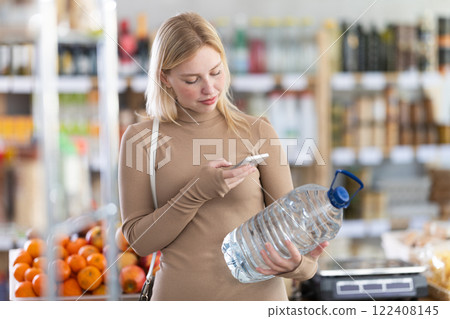 Girl scan QR code, take reading drinking water label using phone camera in shop 122408145