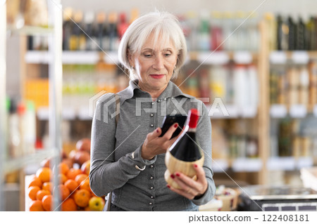 Checking expiration date of wine - elderly female shopper scans QR code on label of wine using smartphone 122408181