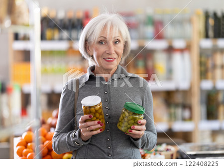 Shopping in produce supermarket - mature fremale buyer makes a choice when buying canned olives 122408225